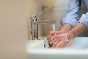 hombre utilizando jabón y Lavado manos debajo el agua grifo. higiene concepto mano de cerca detalle. foto