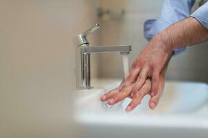 hombre utilizando jabón y Lavado manos debajo el agua grifo. higiene concepto mano de cerca detalle. foto