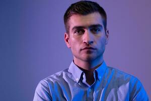 A man in a shirt poses on a dark multicolored neon background photo