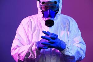 Coronavirus covid-19 pandemic. Doctor scientist wearing protective biological suit and mask due to global healthcare epidemic warning and danger background in blue and pink neon lights background. photo