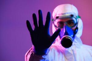 Coronavirus covid-19 pandemic. Doctor scientist wearing protective biological suit and mask due to global healthcare epidemic warning and danger background in blue and pink neon lights background. photo