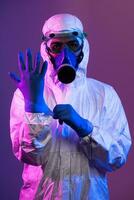 Coronavirus covid-19 pandemic. Doctor scientist wearing protective biological suit and mask due to global healthcare epidemic warning and danger background in blue and pink neon lights background. photo