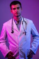 Coronavirus covid-19 danger alert Portrait of hero in white coat. Cheerful smiling young doctor with stethoscope in medical hospital standing against blue and pink background. photo