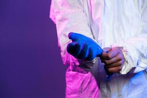 Coronavirus covid-19 pandemic. Doctor scientist wearing protective biological suit and mask due to global healthcare epidemic warning and danger background in blue and pink neon lights background. photo