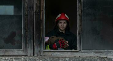 Firefighter hero carrying baby girl out from burning building area from fire incident. Rescue people from dangerous place photo