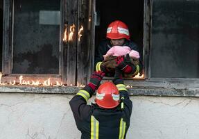 Firefighter hero carrying baby girl out from burning building area from fire incident. Rescue people from dangerous place photo