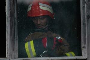 Firefighter hero carrying baby girl out from burning building area from fire incident. Rescue people from dangerous place photo