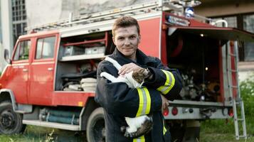 Close-up portrait of heroic fireman in protective suit and red helmet holds saved cat in his arms. Firefighter in fire fighting operation. photo
