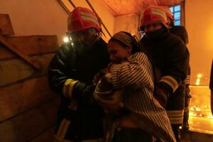 Brave Fireman Descends Stairs of a Burning Building and Holds Saved Girl in His Arms. Open fire and one Firefighter in the Background. photo