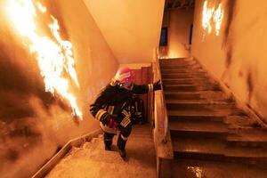 Brave Fireman Descends Stairs of a Burning Building and Holds Saved Girl in His Arms. Open fire and one Firefighter in the Background. photo