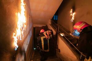 Brave Fireman Descends Stairs of a Burning Building and Holds Saved Girl in His Arms. Open fire and one Firefighter in the Background. photo