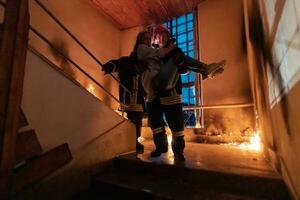 valiente bombero desciende escalera de un ardiente edificio y sostiene salvado niña en su brazos. abierto fuego y uno bombero en el antecedentes. foto