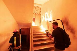 valiente bombero desciende escalera de un ardiente edificio y sostiene salvado niña en su brazos. abierto fuego. cineasta tomando disparar con Pro cine cámara y tres ejes cardán estabilización. bajo ligero foto