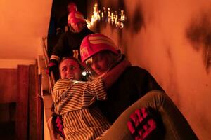 Brave Fireman Descends Stairs of a Burning Building and Holds Saved Girl in His Arms. Open fire and one Firefighter in the Background. photo