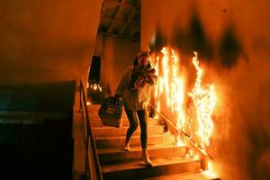 Brave Fireman Descends Stairs of a Burning Building and Holds Saved Girl in His Arms. Open fire and one Firefighter in the Background. photo