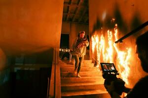 Brave Fireman Descends Stairs of a Burning Building and Holds Saved Girl in His Arms. Open fire and one Firefighter in the Background. photo