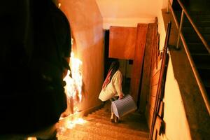 valiente bombero desciende escalera de un ardiente edificio y sostiene salvado niña en su brazos. abierto fuego y uno bombero en el antecedentes. foto