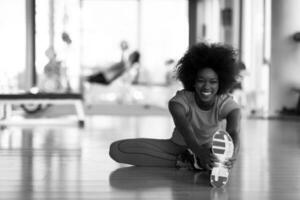 woman in a gym stretching and warming up man in background working with dumbbels photo