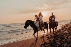 The family spends time with their children while riding horses together on a sandy beach. Selective focus photo