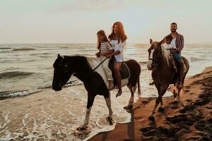 The family spends time with their children while riding horses together on a sandy beach. Selective focus photo