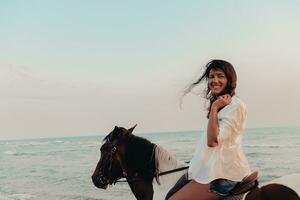 Woman in summer clothes enjoys riding a horse on a beautiful sandy beach at sunset. Selective focus photo