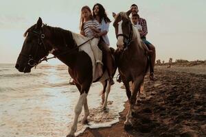 The family spends time with their children while riding horses together on a sandy beach. Selective focus photo