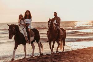 The family spends time with their children while riding horses together on a sandy beach. Selective focus photo