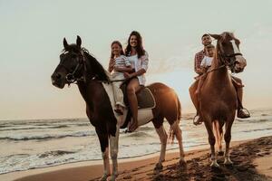 The family spends time with their children while riding horses together on a sandy beach. Selective focus photo