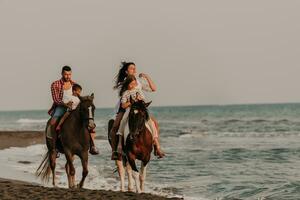 The family spends time with their children while riding horses together on a sandy beach. Selective focus photo