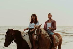 A loving couple in summer clothes riding a horse on a sandy beach at sunset. Sea and sunset in the background. Selective focus photo