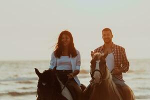 A loving couple in summer clothes riding a horse on a sandy beach at sunset. Sea and sunset in the background. Selective focus photo