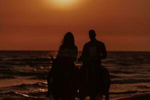 una pareja amorosa vestida de verano montando a caballo en una playa de arena al atardecer. mar y puesta de sol de fondo. enfoque selectivo foto