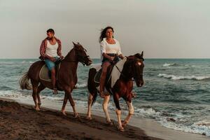 A loving couple in summer clothes riding a horse on a sandy beach at sunset. Sea and sunset in the background. Selective focus photo