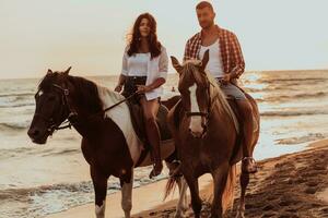 A loving couple in summer clothes riding a horse on a sandy beach at sunset. Sea and sunset in the background. Selective focus photo