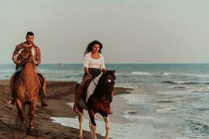 una pareja amorosa vestida de verano montando a caballo en una playa de arena al atardecer. mar y puesta de sol de fondo. enfoque selectivo foto