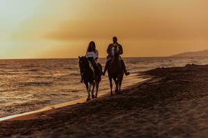 una pareja amorosa vestida de verano montando a caballo en una playa de arena al atardecer. mar y puesta de sol de fondo. enfoque selectivo foto