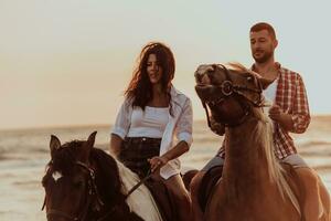 A loving couple in summer clothes riding a horse on a sandy beach at sunset. Sea and sunset in the background. Selective focus photo