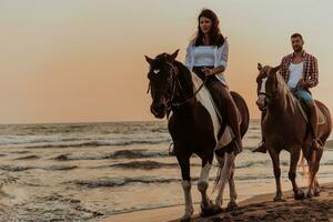 A loving couple in summer clothes riding a horse on a sandy beach at sunset. Sea and sunset in the background. Selective focus photo