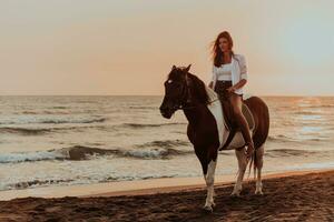 Woman in summer clothes enjoys riding a horse on a beautiful sandy beach at sunset. Selective focus photo