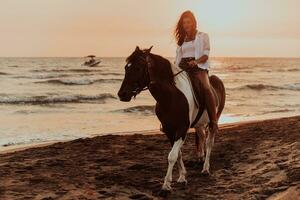 Woman in summer clothes enjoys riding a horse on a beautiful sandy beach at sunset. Selective focus photo