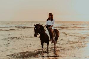 Woman in summer clothes enjoys riding a horse on a beautiful sandy beach at sunset. Selective focus photo