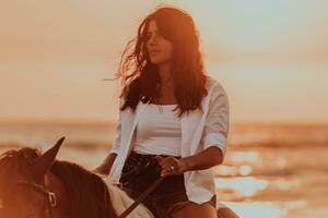 Woman in summer clothes enjoys riding a horse on a beautiful sandy beach at sunset. Selective focus photo