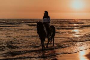 Woman in summer clothes enjoys riding a horse on a beautiful sandy beach at sunset. Selective focus photo