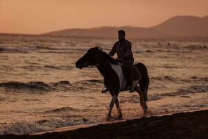 un hombre moderno con ropa de verano disfruta montando a caballo en una hermosa playa de arena al atardecer. enfoque selectivo foto