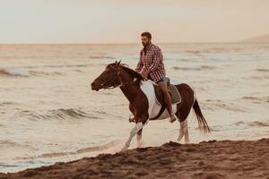 un hombre moderno con ropa de verano disfruta montando a caballo en una hermosa playa de arena al atardecer. enfoque selectivo foto