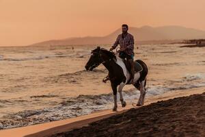 un hombre moderno con ropa de verano disfruta montando a caballo en una hermosa playa de arena al atardecer. enfoque selectivo foto