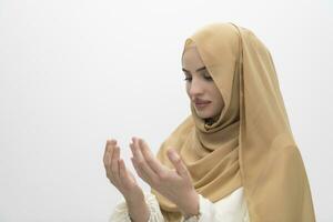 portrait of beautiful muslim woman in fashionable dress with hijab making traditional prayer to God keeps hands in praying gesture isolated on white background photo