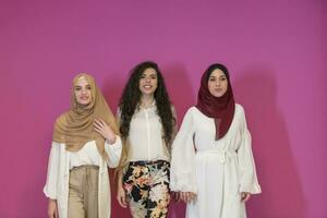 three Muslim women in hijab in a modern clothes pose against a pink background photo