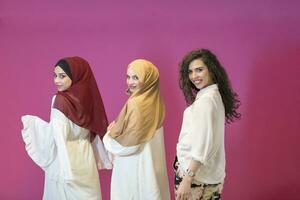 grupo retrato de hermosa musulmán mujer dos de ellos en un de moda vestir con hijab aislado en un rosado antecedentes foto