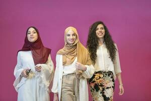 three Muslim women in hijab in a modern clothes pose against a pink background photo